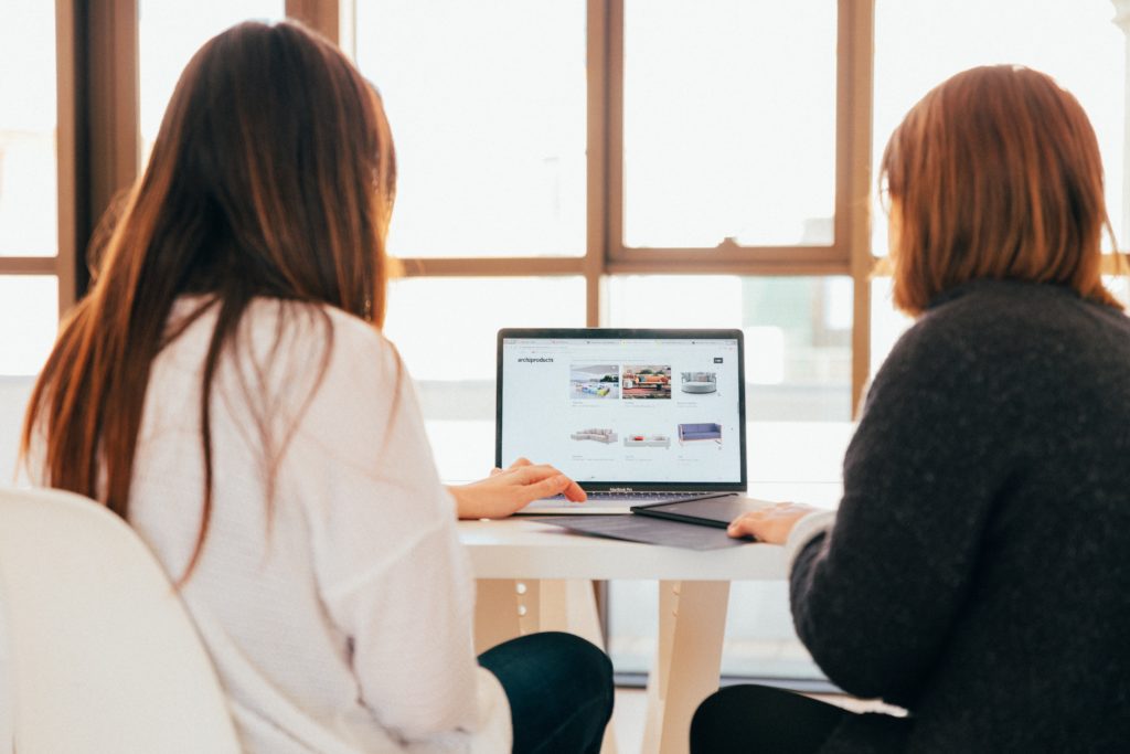 Deux femmes sont assises devant un ordinateur ouvert. Elles travaillent ensemble dessus.